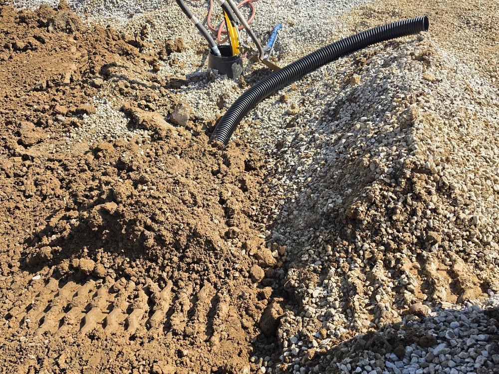 A hand-cut drainage trench through gravel and soil, shaped to carry water away.