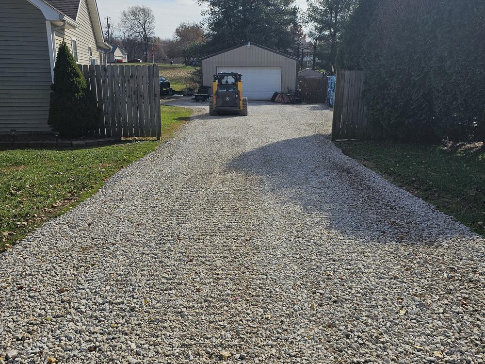A newly regraded gravel driveway running alongside a house, with the edges squared and the surface compacted.