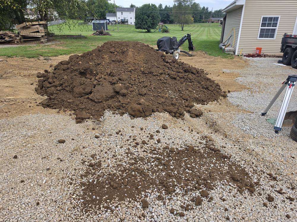 A dirt pile beside an existing driveway where new material has been delivered and spread across the surface.